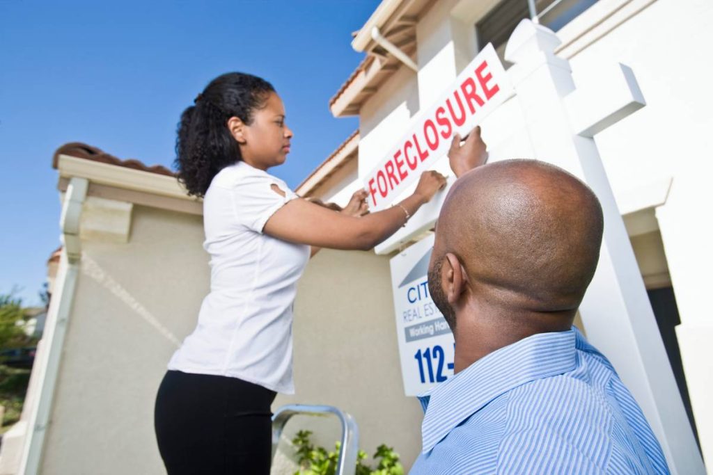 Couple putting up a foreclosure sign outside a house