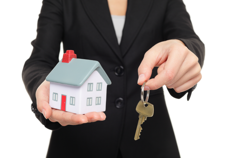 A Bastrop real estate agent holding the key to a new house next to a miniature house model.