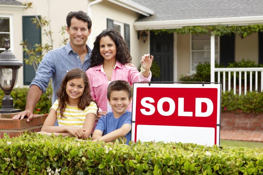 Happy family embracing in front of their new home in a charming neighborhood - Discover homes for sale in Caldwell County TX