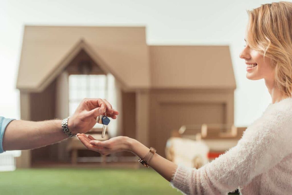 Lockhart realtors handing keys to a happy homeowner in front of a model house.