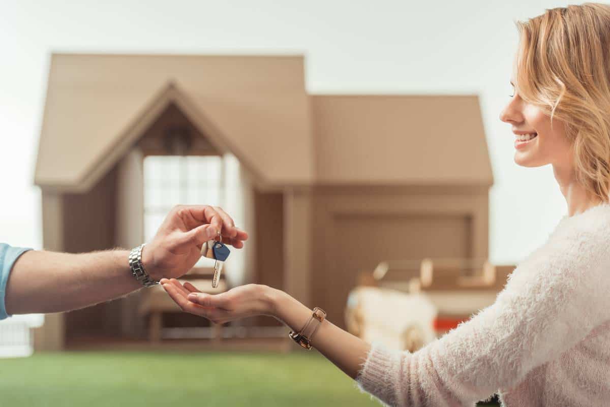 Lockhart realtors handing keys to a happy homeowner in front of a model house.