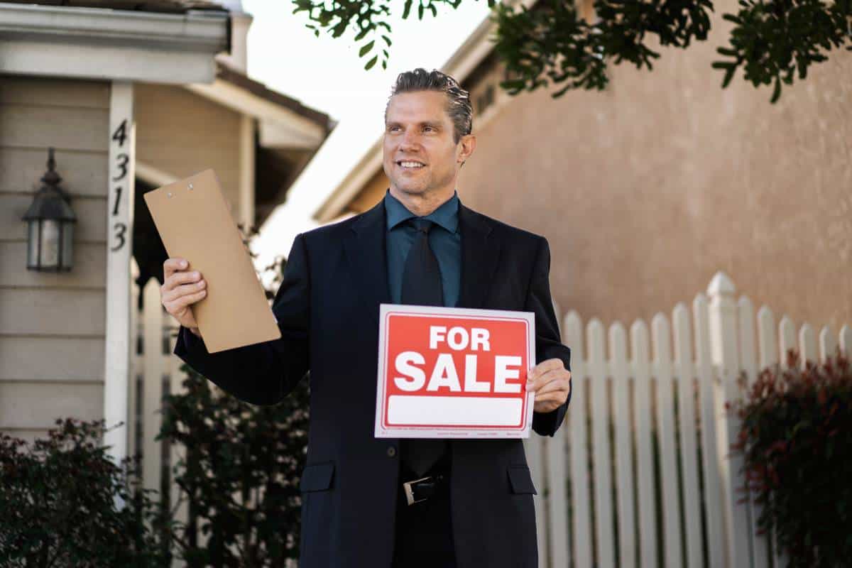 A realtor holding a For Sale sign in front of a home for sale in Lockhart.