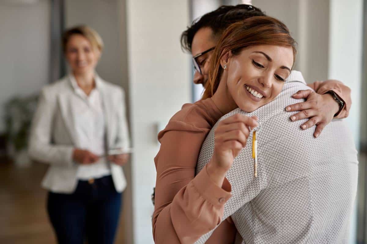 A couple hugs, holding keys after Luling realtors helped them close a deal on their new home.