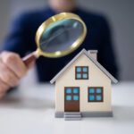 A concept of Lockhart realty with a person holding a magnifying glass inspecting a small model house.