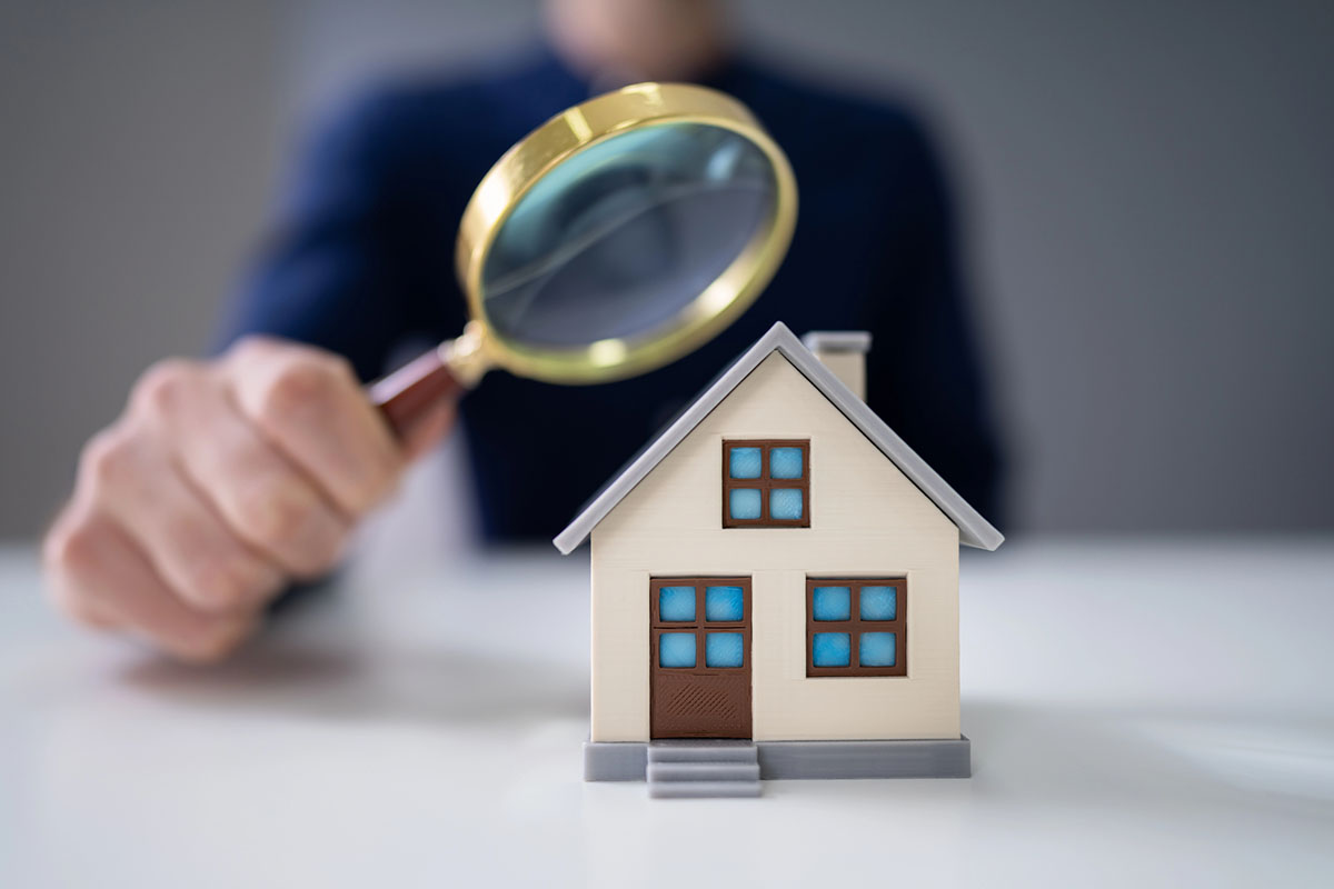 A concept of Lockhart realty with a person holding a magnifying glass inspecting a small model house.