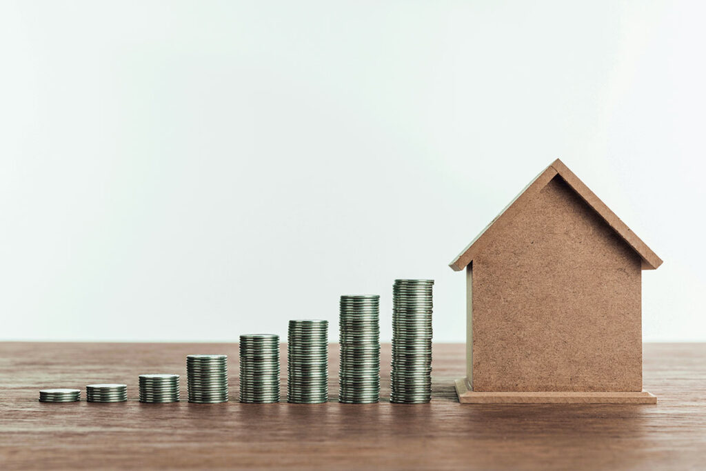 A cardboard house model and coin stacks symbolizing Lockhart real estate investment opportunities.