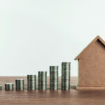 A cardboard house model and coin stacks symbolizing Lockhart real estate investment opportunities.