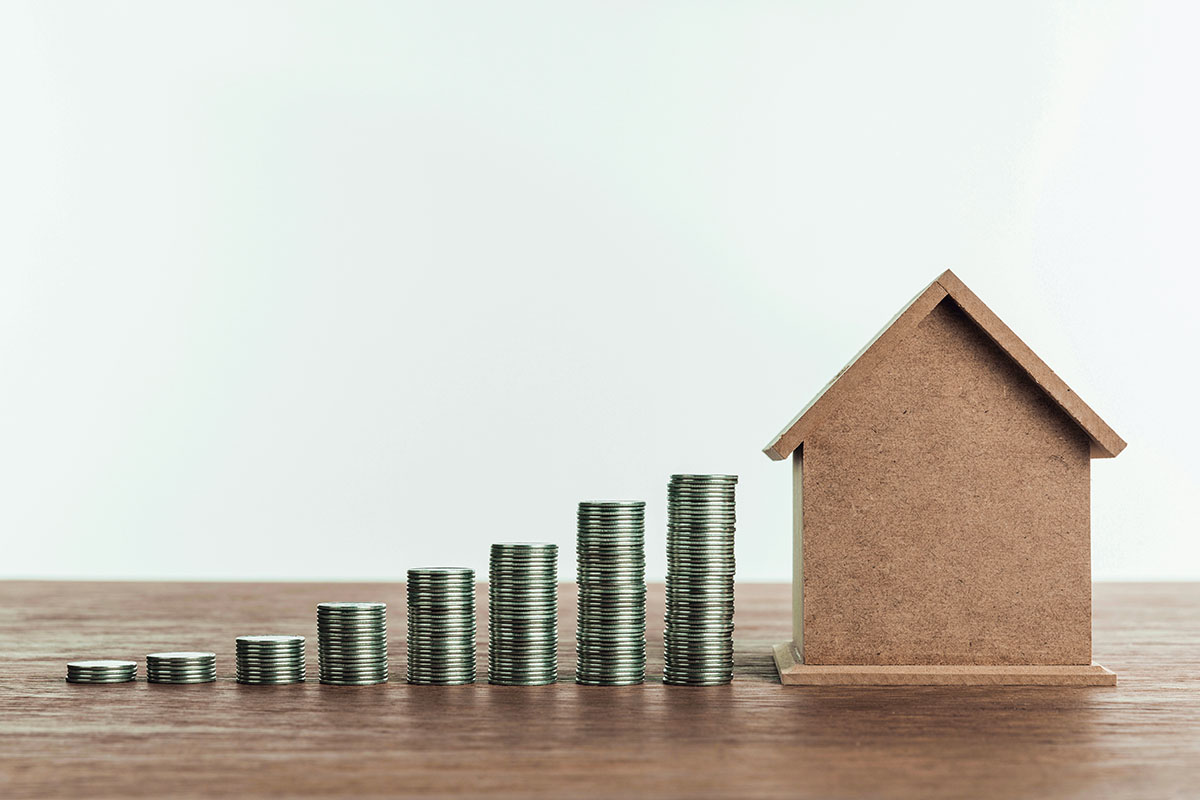 A cardboard house model and coin stacks symbolizing Lockhart real estate investment opportunities.