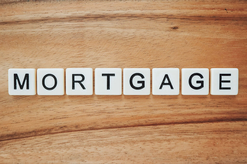 Scrabble blocks spell the word "MORTGAGE" on a wooden table.