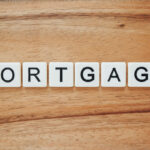 Scrabble blocks spell the word "MORTGAGE" on a wooden table.