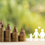 A paper cutout of a family is standing next to a series of steps created by coins with a house at the top.
