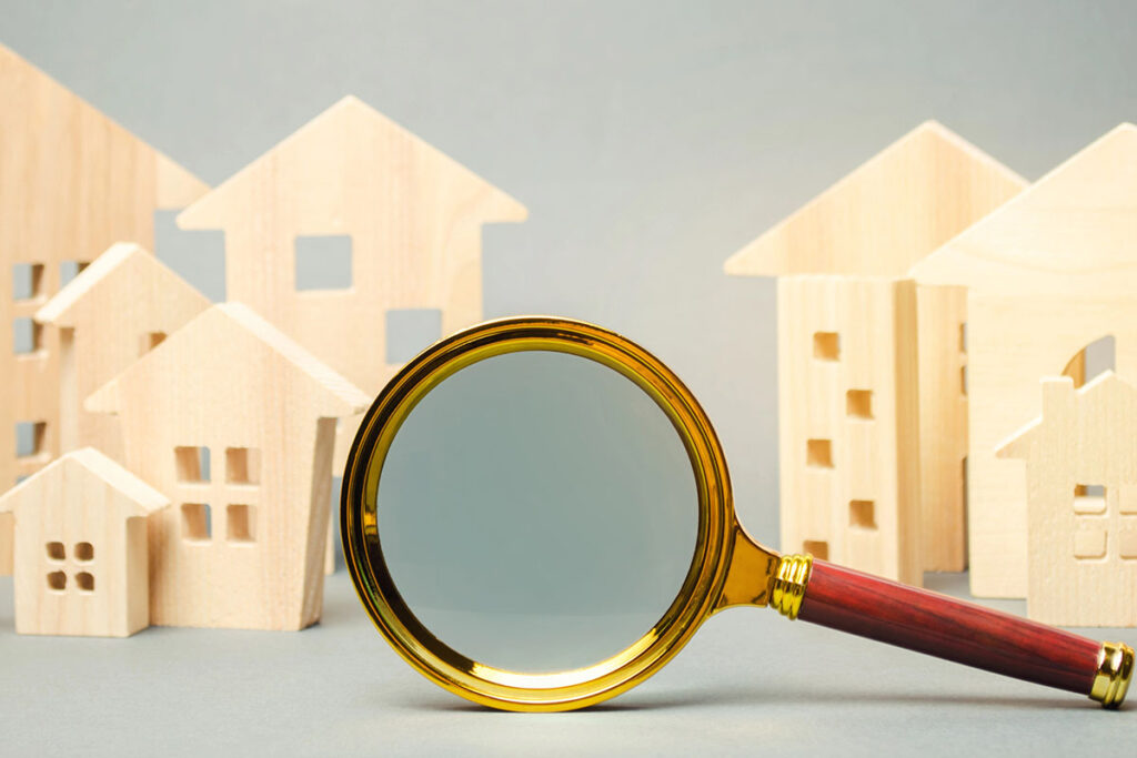 A gold and wooden magnifying glass in the foreground, focusing on a collection of small wooden house models in the background.