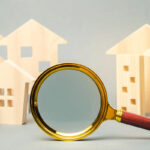 A gold and wooden magnifying glass in the foreground, focusing on a collection of small wooden house models in the background.