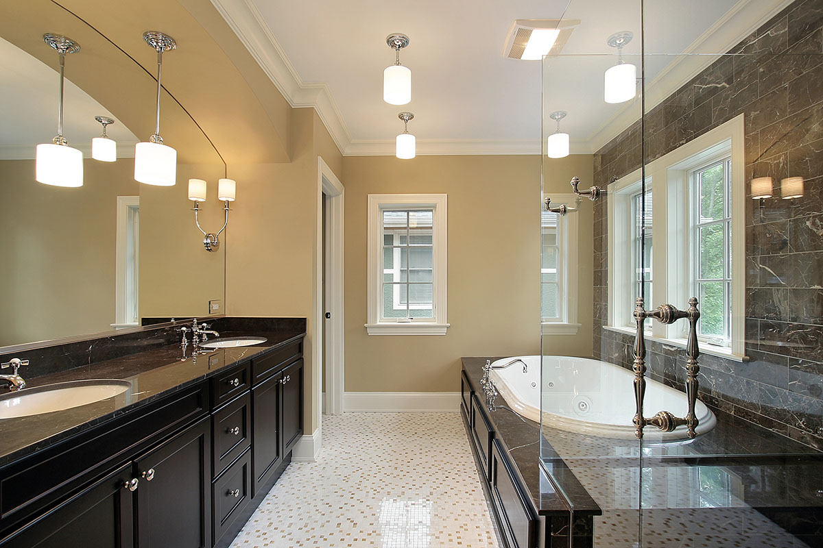 A stylish bathroom featuring a dark wood vanity with two sinks, a large white soaking tub, and marble accents. The walls are painted a soft beige, complemented by lighting fixtures and large windows that provide natural light. The floor is adorned with polished tiles in a mosaic pattern.