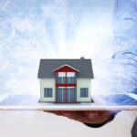 A miniature model house resting on a white tablet held in a person's hand, overlaid with a glowing blue digital network and binary code.