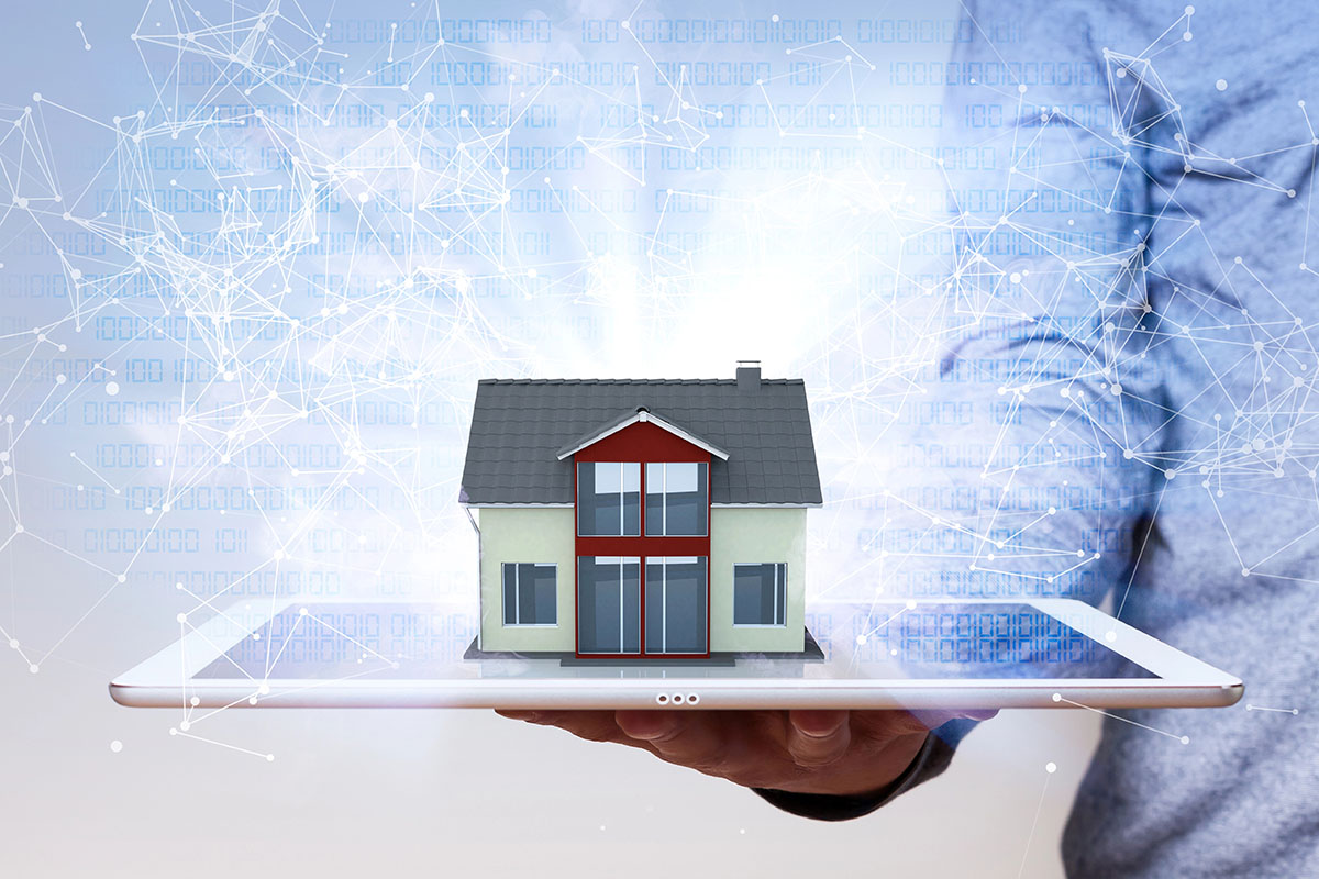 A miniature model house resting on a white tablet held in a person's hand, overlaid with a glowing blue digital network and binary code.